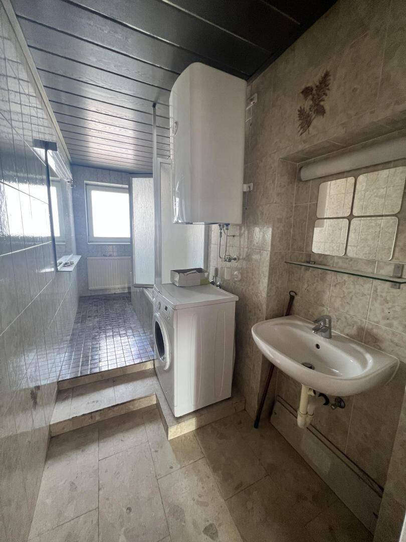Badezimmer mit Fliesen, Waschmaschine, Waschbecken und Duschbereich.