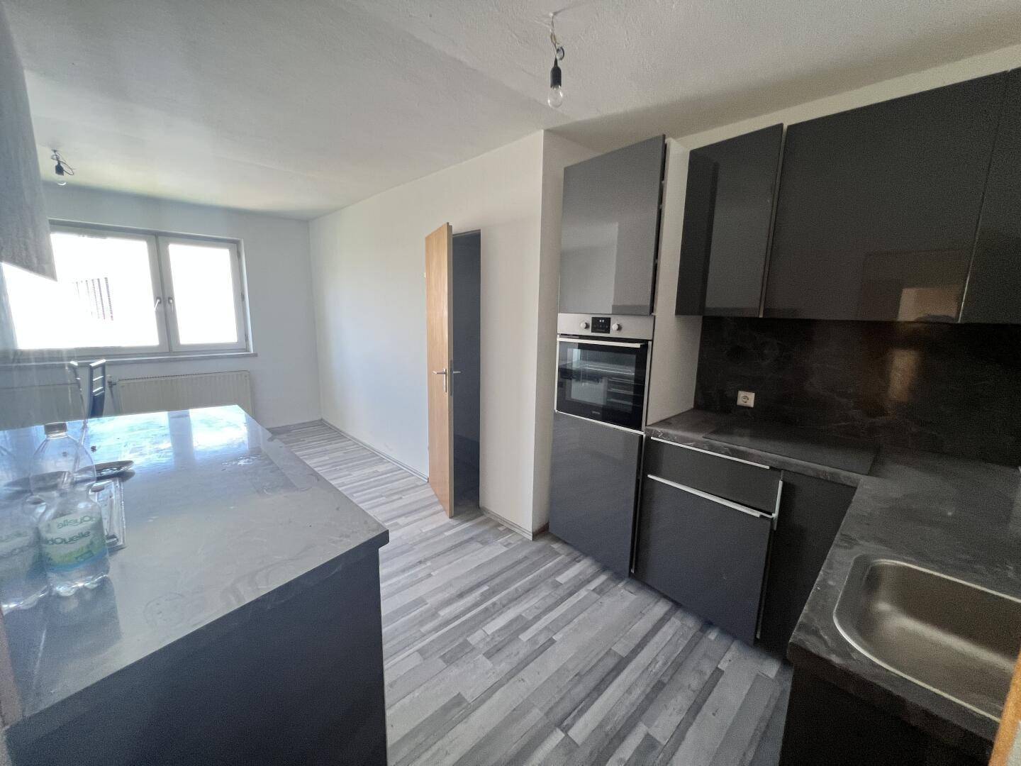 Moderne Küche mit dunkelgrauen Schränken, Einbauofen und Laminatboden.