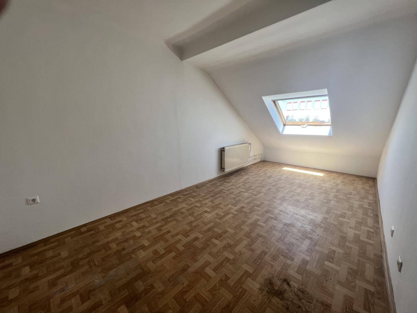 Helles Dachzimmer mit schrägen Wänden, Parkettboden und Dachfenster.