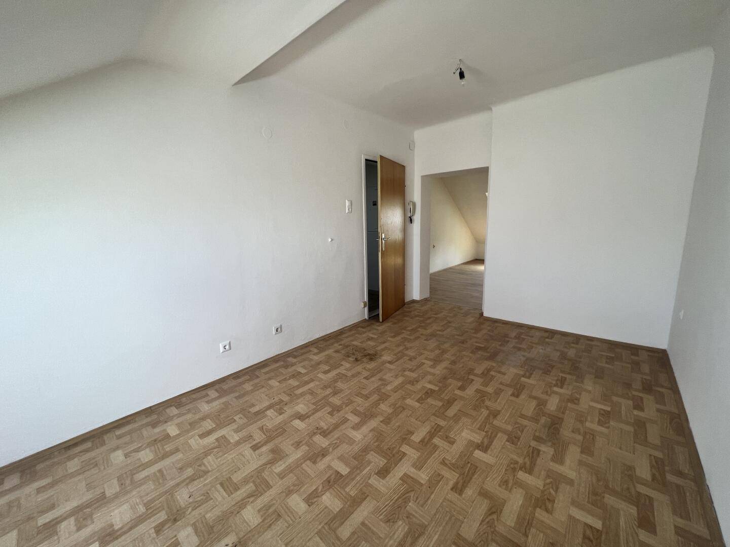 Geräumiges Dachzimmer mit Parkettboden und Zugang zu weiteren Räumen.