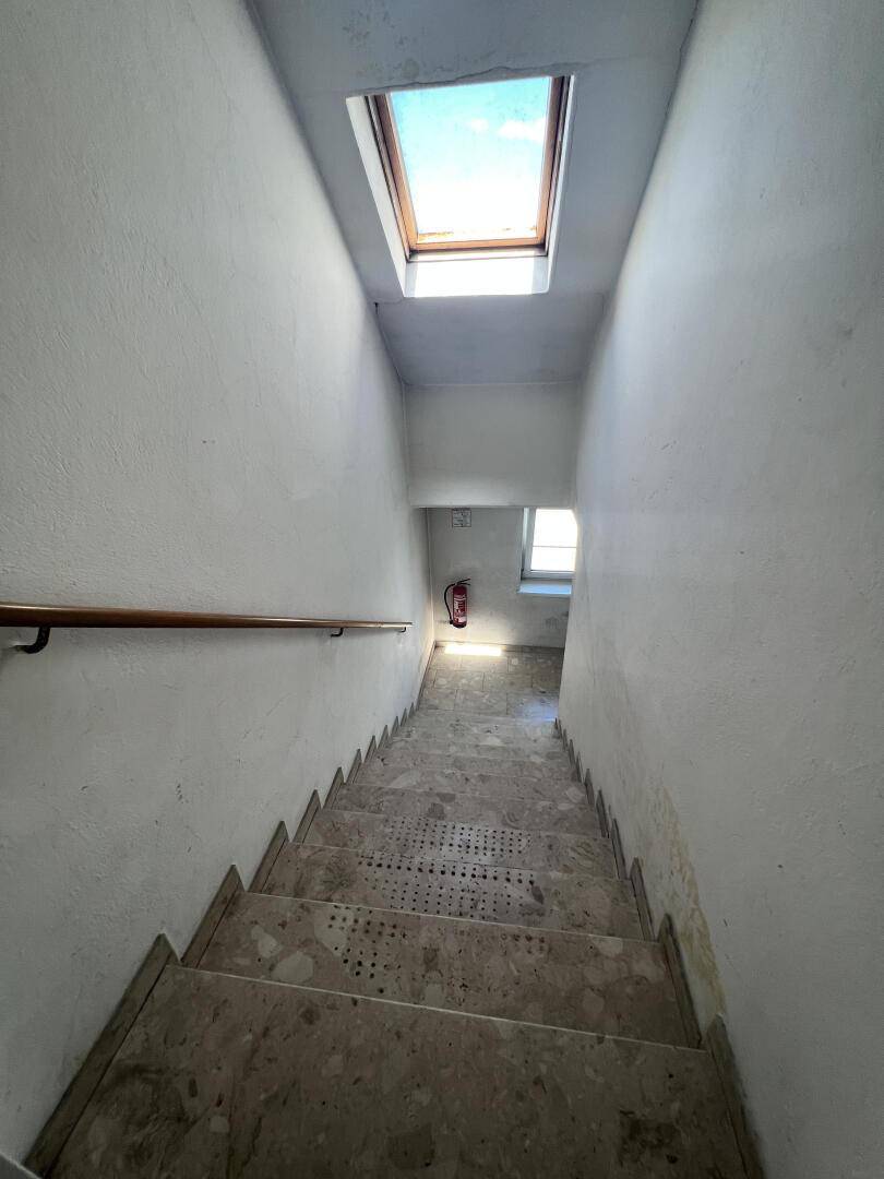 Treppenhaus mit Steinstufen, Holzgeländer und natürlichem Licht durch ein Dachfenster.