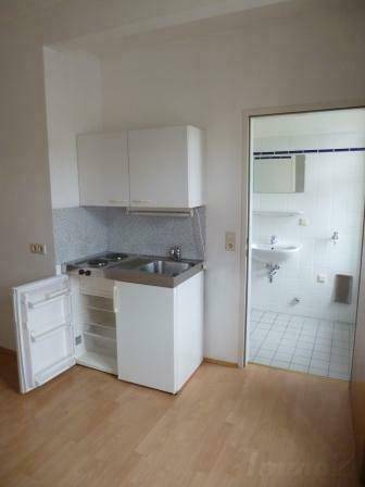 Kompakte Küchenzeile mit Spüle, Kochfeld und Kühlschrank, direkt neben dem Badezimmerzugang.