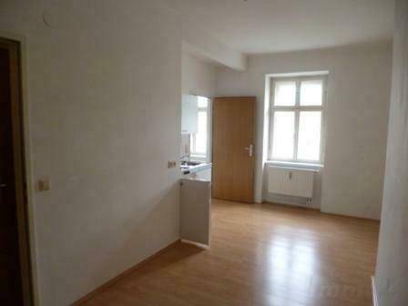 Heller Wohnbereich mit Laminatboden und Fenster, angrenzend an eine kleine Küchenzeile.