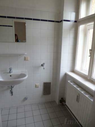 Helles Badezimmer mit Fenster, Waschbecken und weißen Fliesen mit blauer Akzentlinie.