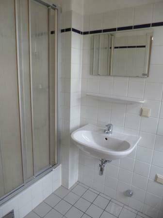 Badezimmer mit Duschkabine, Waschbecken und weiß gefliesten Wänden mit blauer Bordüre.