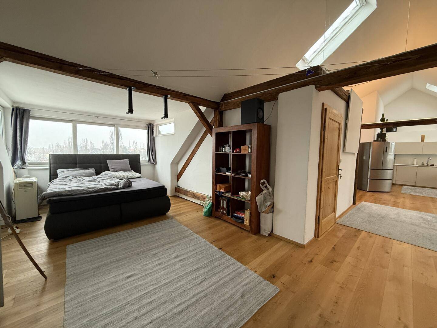 Schlafzimmer mit Holzboden und offenem Zugang zum Wohn- und Küchenbereich.