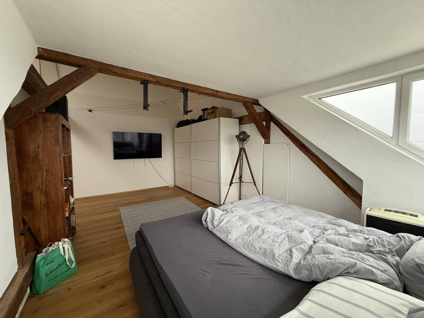 Schlafzimmer mit Fernseher an der Wand, Kleiderschrank und gemütlicher Dachschräge.
