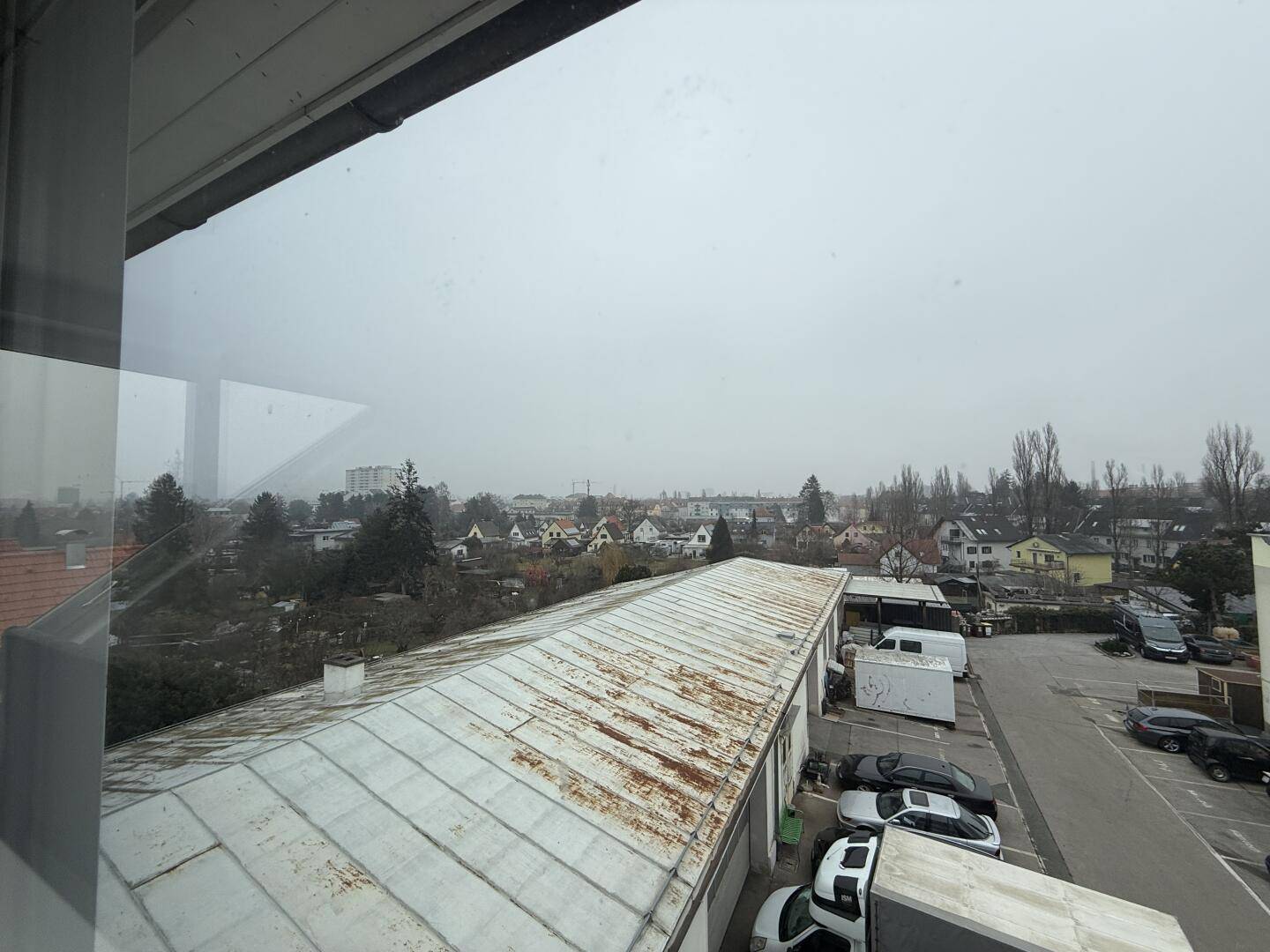 Weitblick aus dem Fenster auf die Dächer, Bäume und die umliegende Bebauung an einem bewölkten Tag.