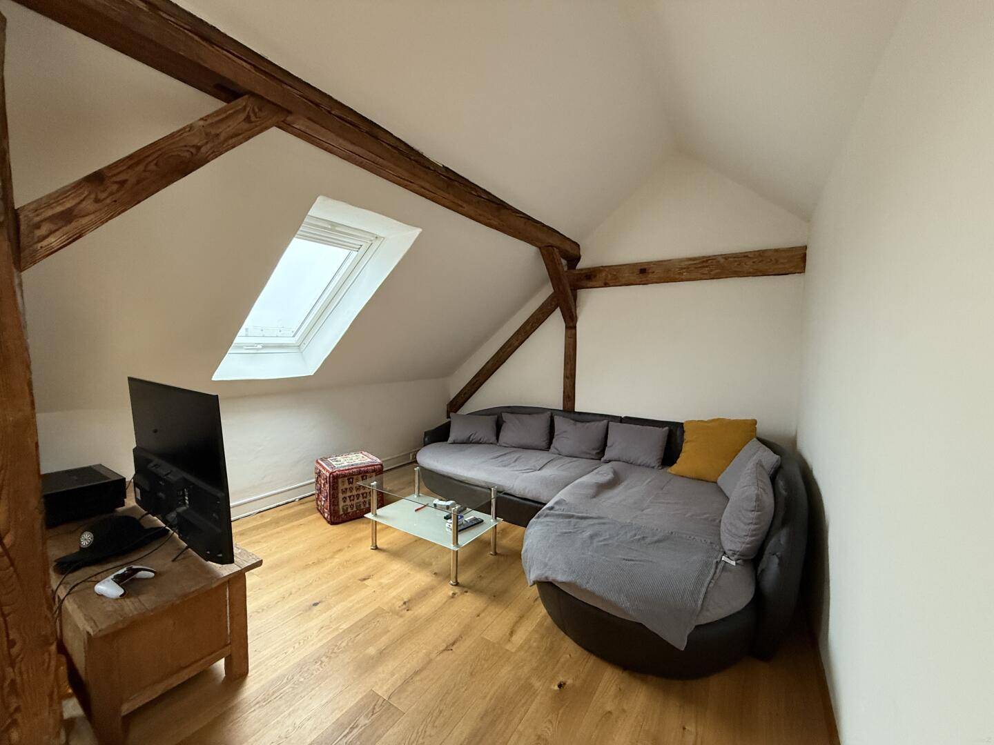 Gemütlicher Wohnbereich unter der Dachschräge mit Sofa, Fernseher und sichtbaren Holzbalken.