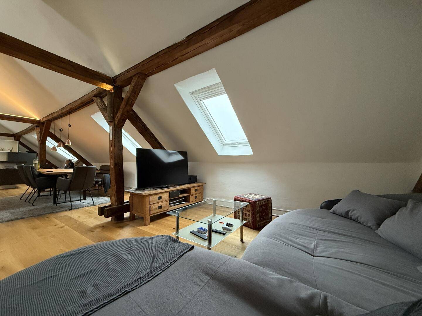 Offener Wohnbereich mit Sofa und Blick auf den Essbereich und die rustikalen Holzbalken.