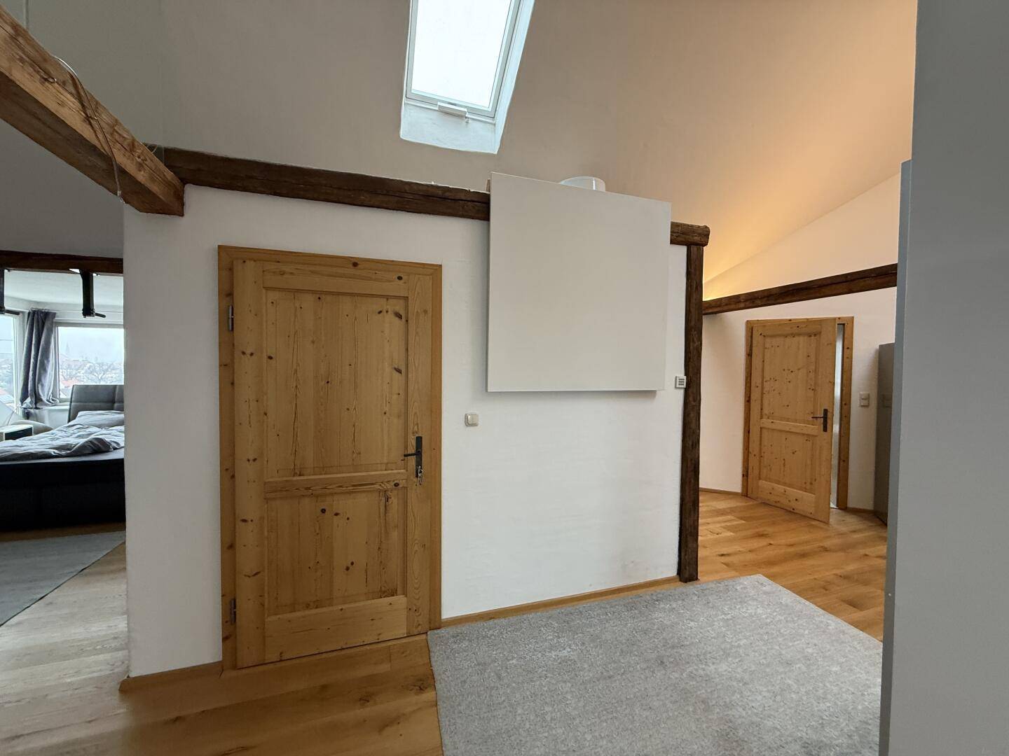 Flur mit rustikaler Holztür, weißen Wänden, sichtbaren Holzbalken und Holzfußboden.