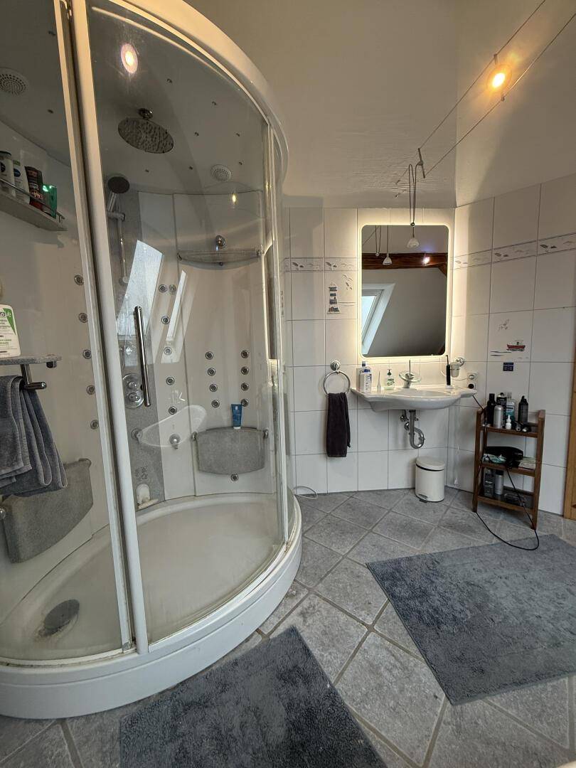 Moderne Duschkabine mit mehreren Düsen und beleuchtetem Spiegel im Badezimmer.