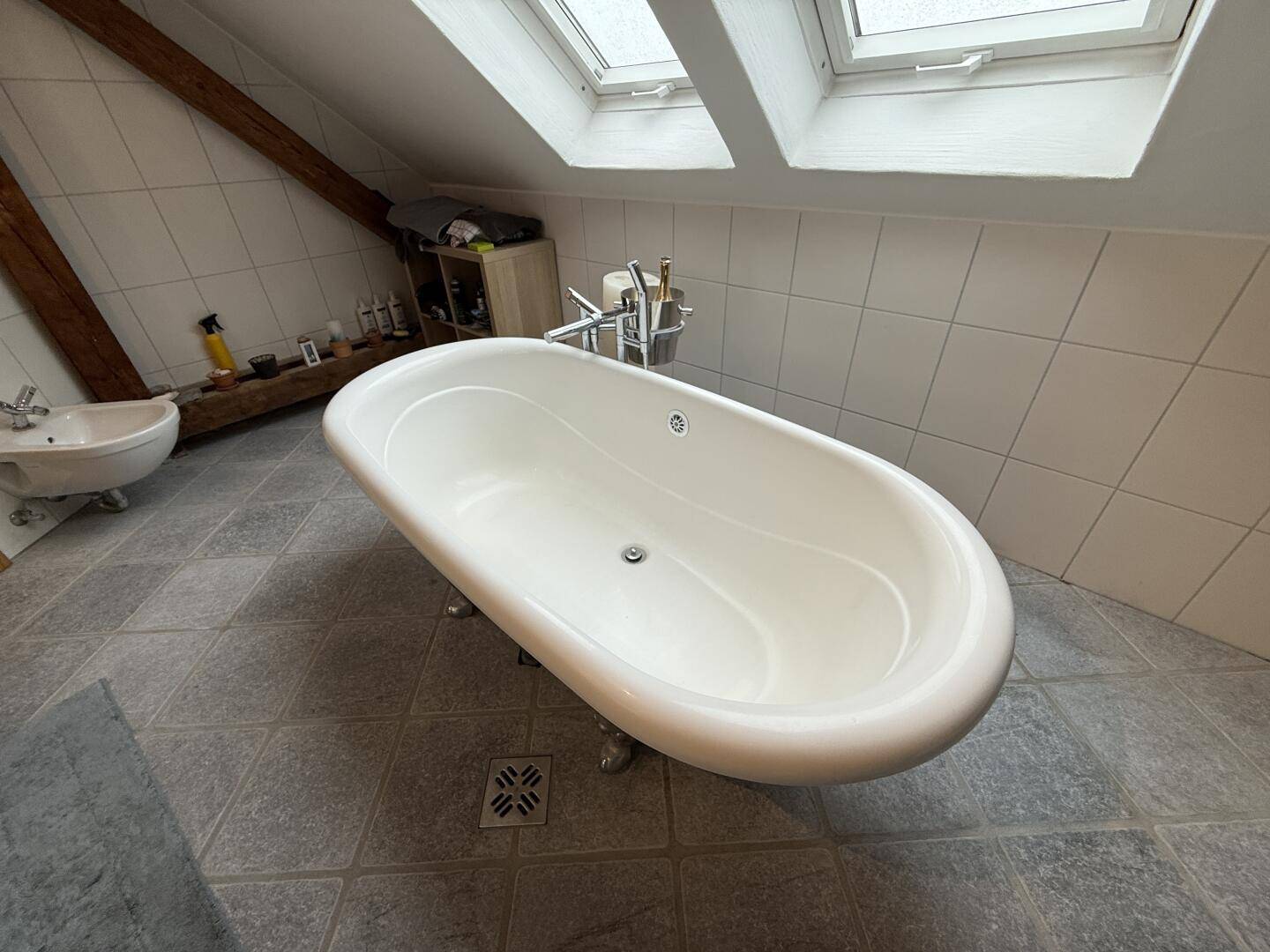 Freistehende Badewanne mit Klauenfüßen und Fliesenboden unter der Dachschräge.