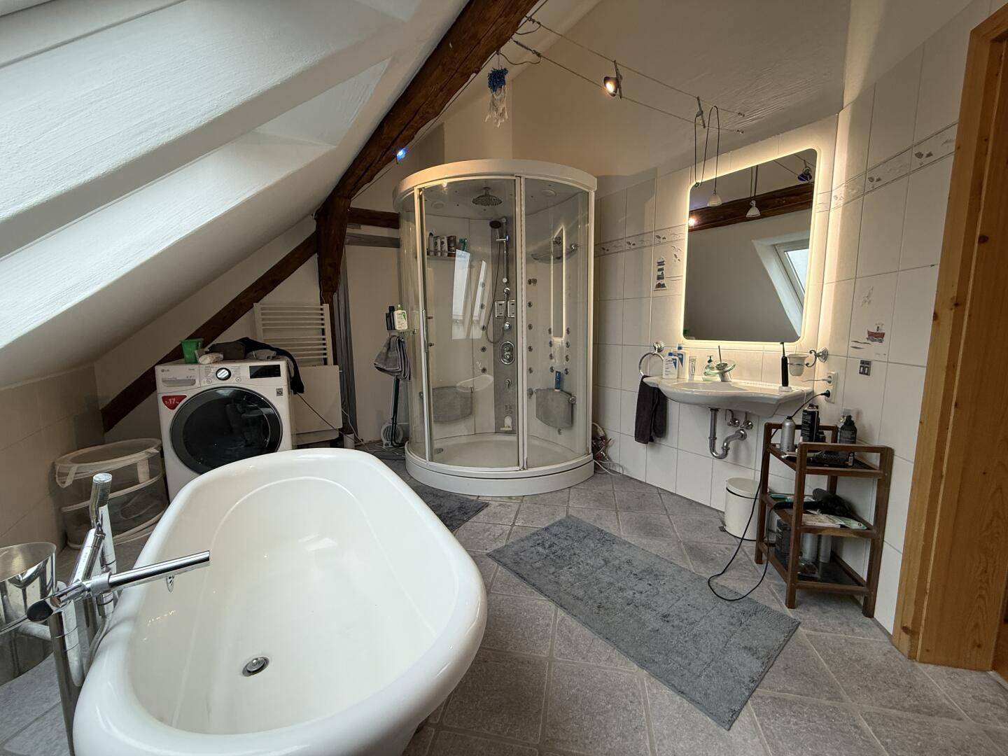 Helles Badezimmer mit freistehender Badewanne, Duschkabine, Waschmaschine und Dachfenstern.
