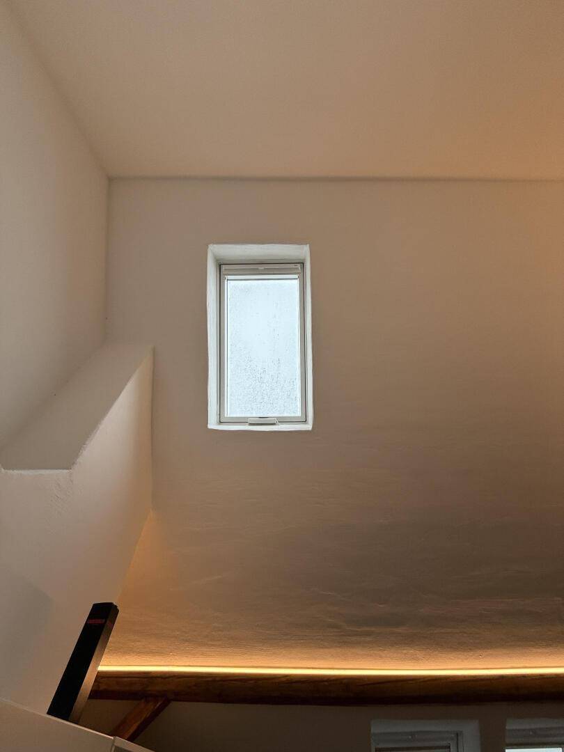 Kleines Fenster in einer weißen Wand, das natürliches Licht in den Raum lässt.