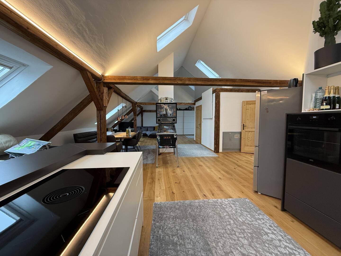 Moderne Küche mit Induktionskochfeld, offen zum Wohnbereich, mit Holzbalken und Dachfenstern.