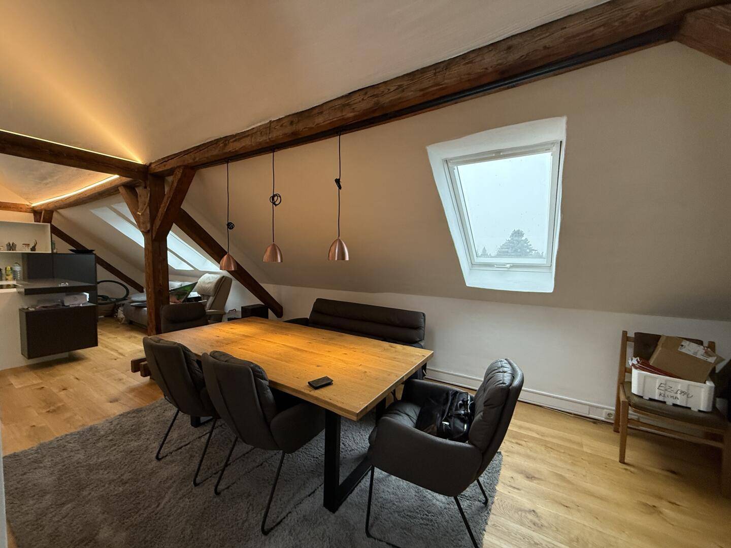 Heller Essbereich mit Holztisch, Dachfenster und Blick auf die umliegende Landschaft.