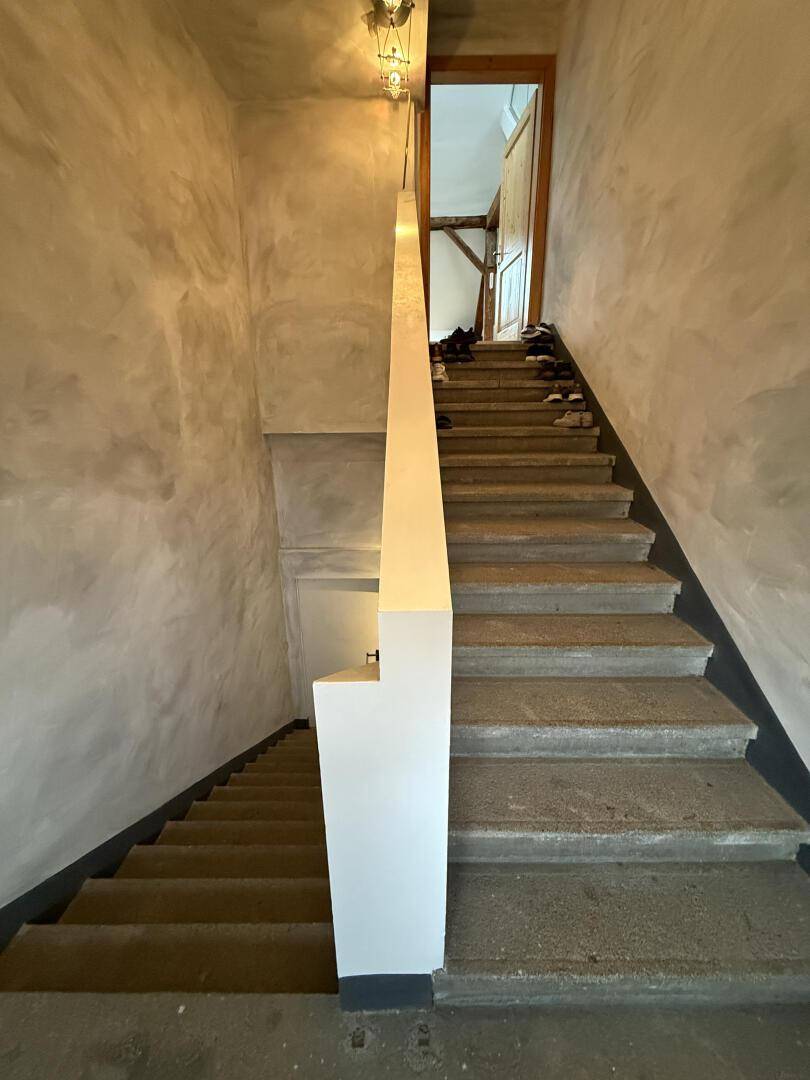 Betontreppe mit strukturierten Wänden und einfacher Beleuchtung, die in die obere Etage führt.