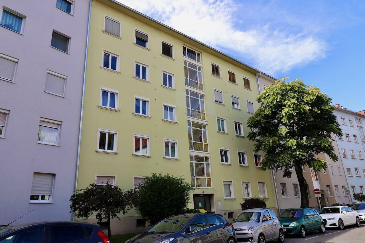 Mehrfamilienhaus mit hellgrüner Fassade, vielen Fenstern und Bäumen davor.