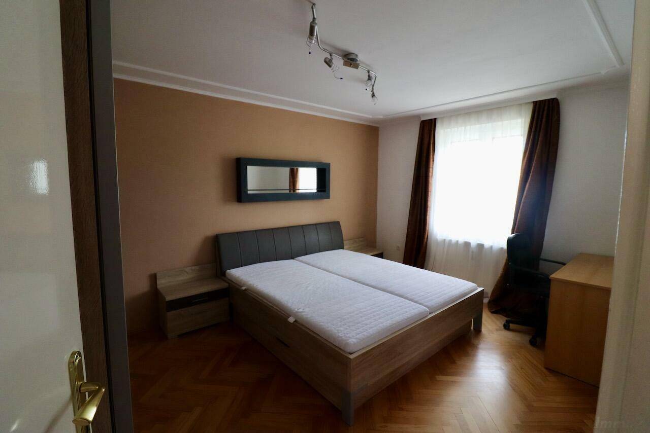 Helles Schlafzimmer mit Parkettboden, Doppelbett und Fenster mit braunen Vorhängen.