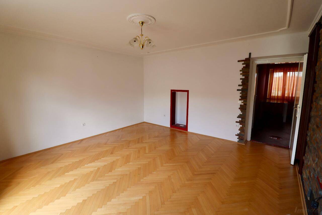 Leeres Wohnzimmer mit Fischgrätparkett, Stuckdecke und rotem Akzentbereich.