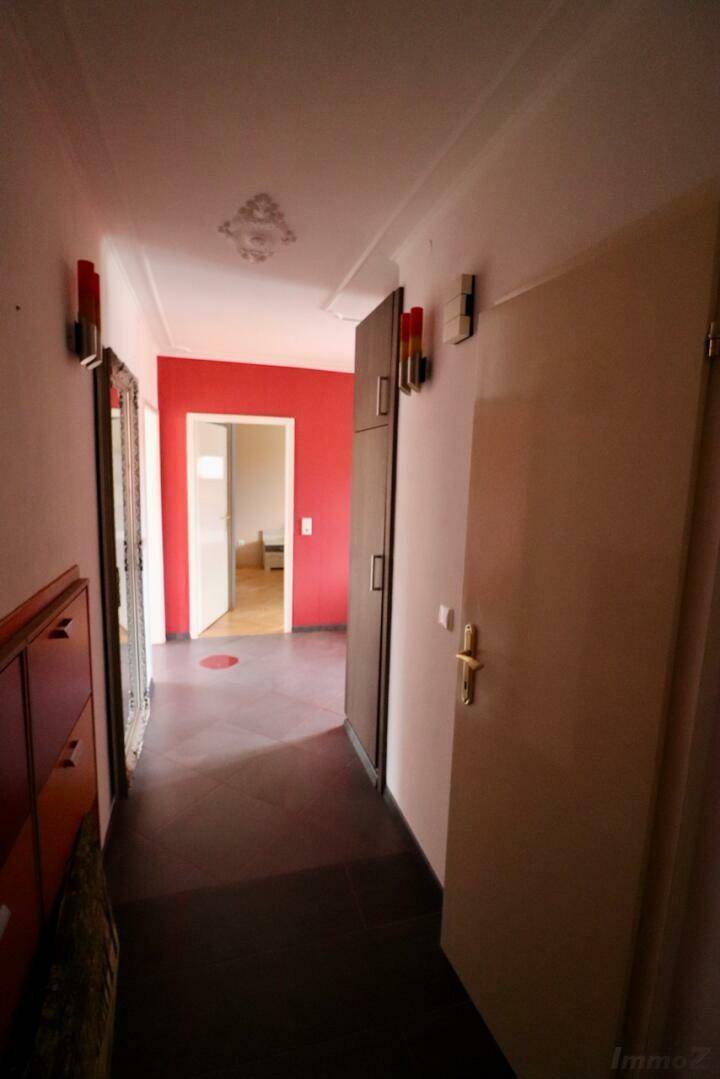 Langer Flur mit dunklem Fliesenboden, roten Akzentwänden und Spiegelschrank.