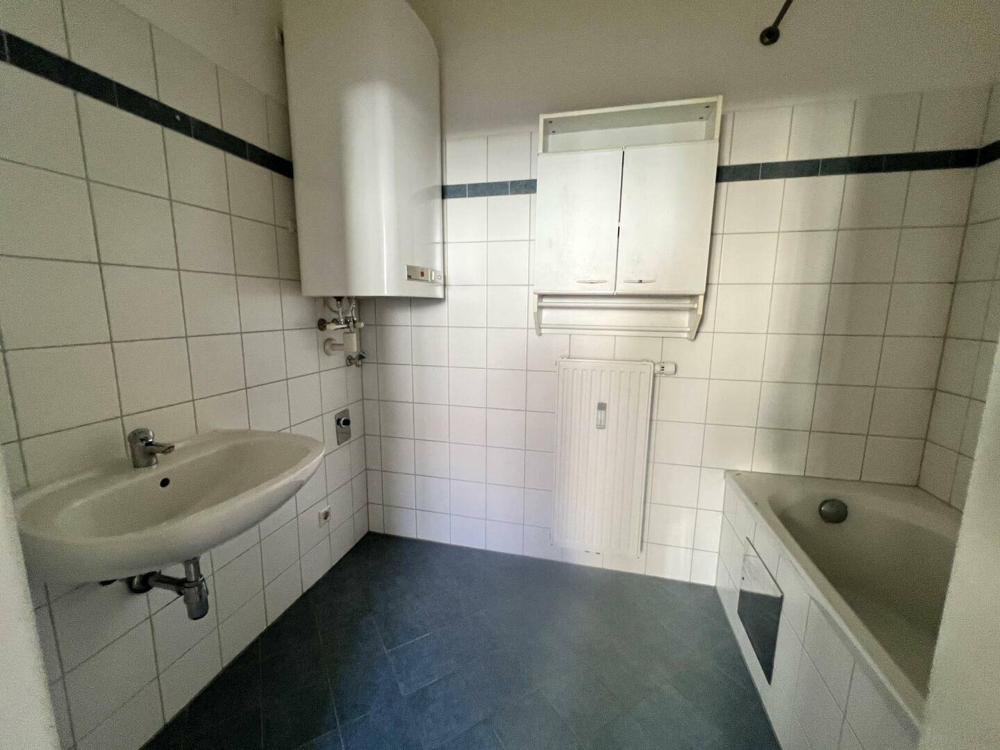 Badezimmer mit Badewanne, Waschbecken und weißen Wandfliesen mit blauen Akzentstreifen.
