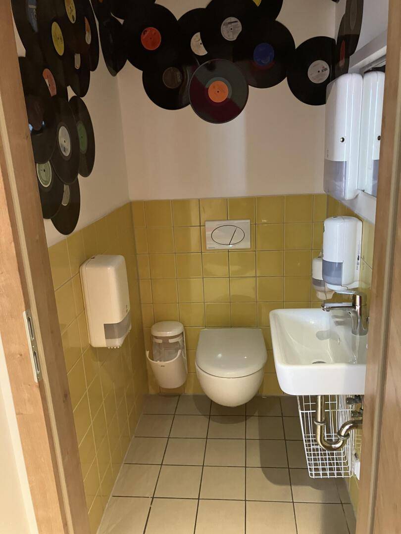 Kleine Toilette mit gelben Fliesen, weißer Keramik und kreativer Wanddekoration mit Schallplatten, einzigartiges Design.