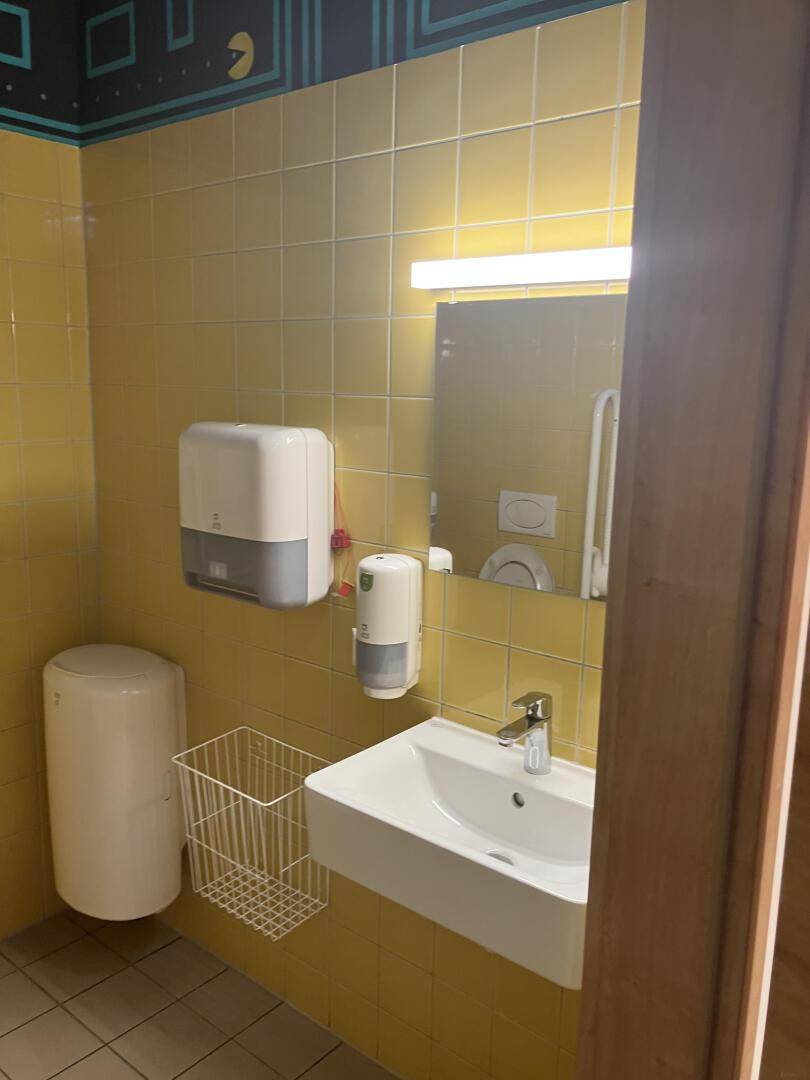 Toilette mit gelben Fliesen, Waschbecken und Spiegel, ausgestattet mit Seifenspendern, sauber und hell.