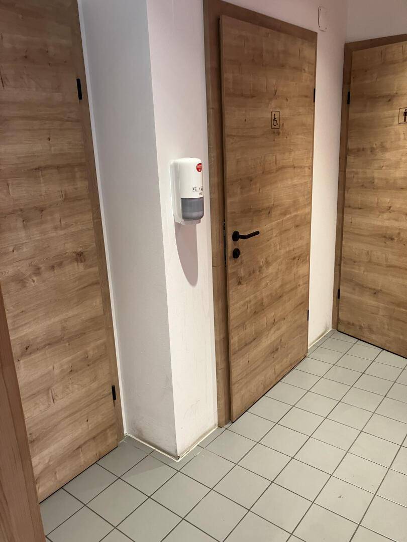 Flur mit Holztüren zu den Toiletten, gekennzeichnet mit Piktogrammen für Barrierefreiheit, sauber und hell.