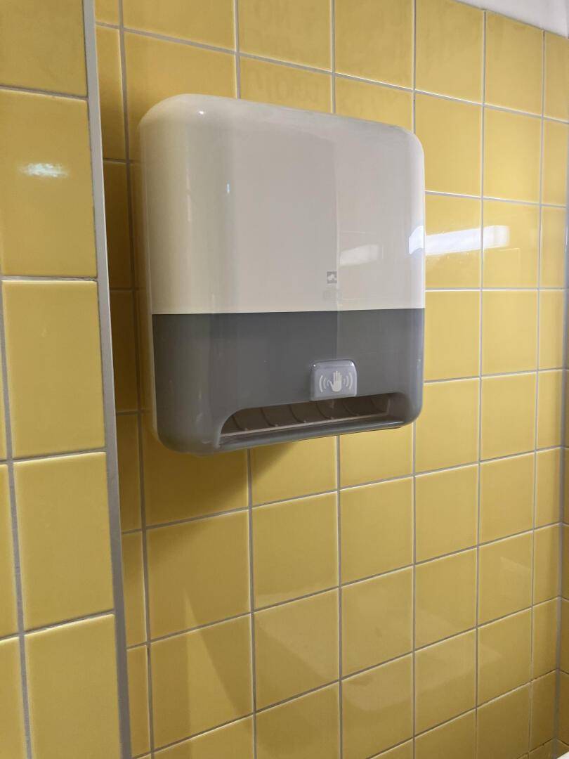 Detailansicht eines Seifenspenders an einer gelb gefliesten Wand in der Toilette, hygienisch und praktisch.