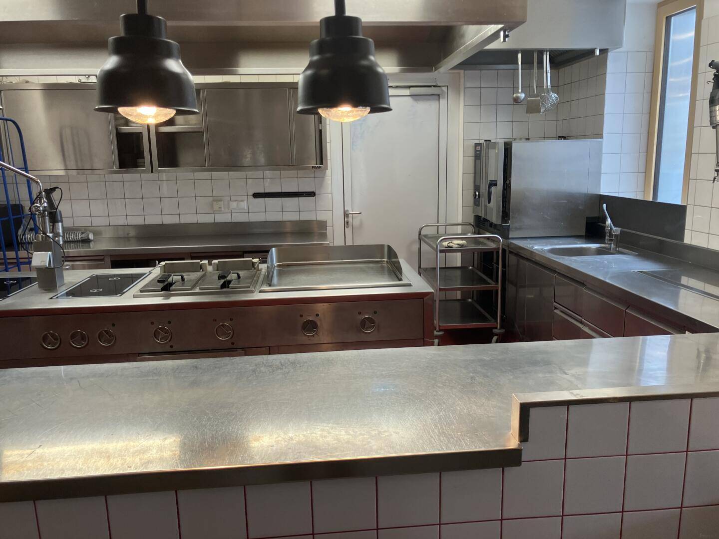 Professionelle Küche mit großer Kochinsel aus Edelstahl, weißen Fliesen und Ablufthaube, modern und funktional.