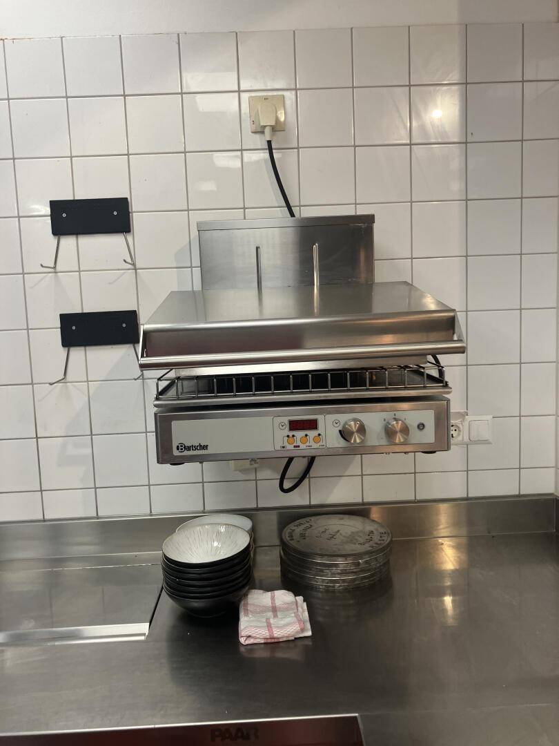 Wandmontierter Grill oder Salamander über einer Edelstahlarbeitsfläche in der Küche, professionelle Ausstattung.