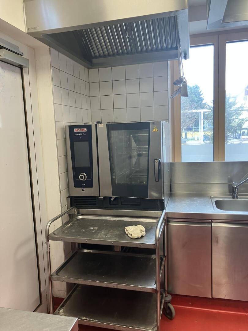 Professionelle Öfen und ein Servierwagen in der Großküche, mit Fenster und Edelstahlspüle, gut organisiert.
