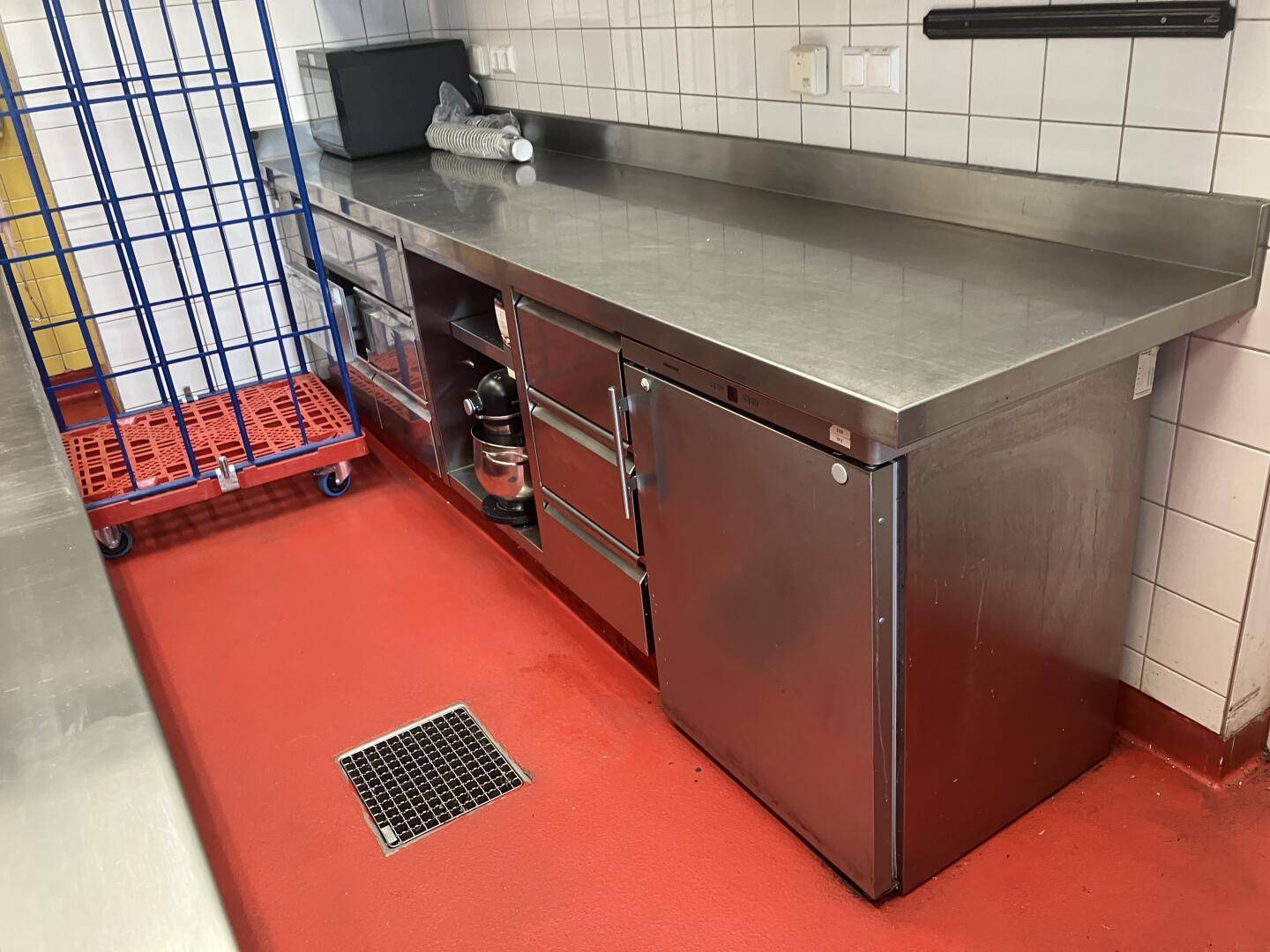 Edelstahlarbeitsfläche mit integriertem Kühlschrank und rotem Boden in der professionellen Küche, funktional.