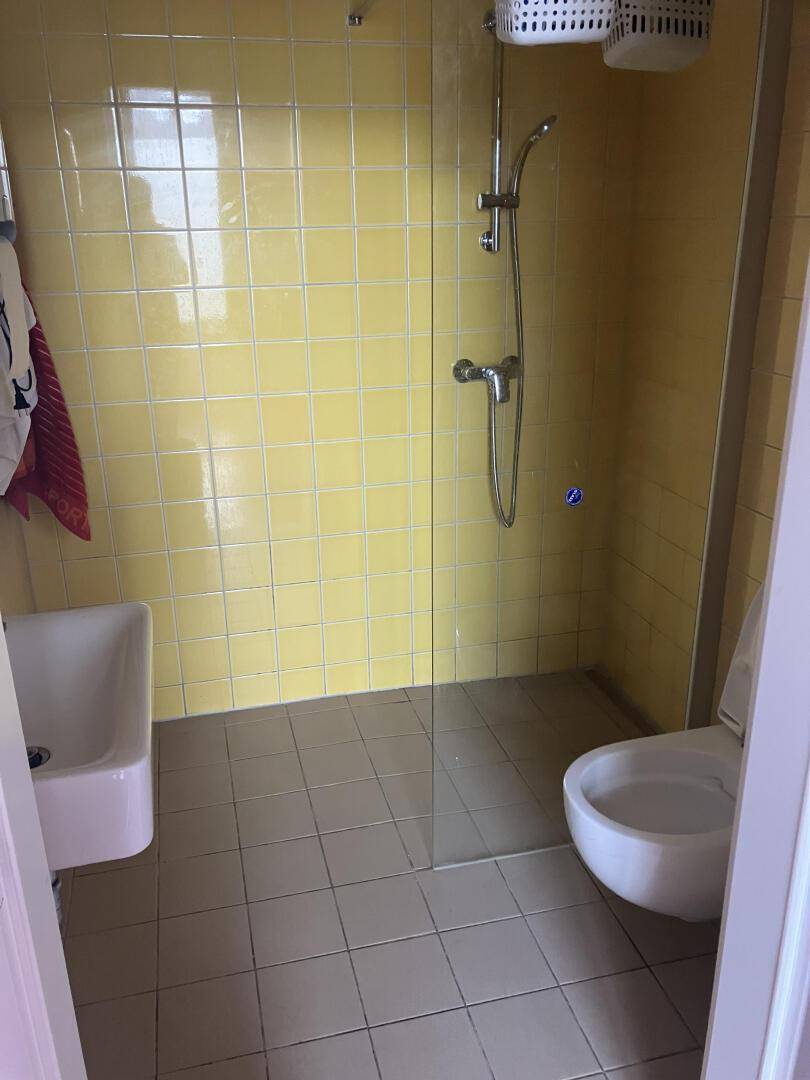 Duschraum mit gelben Fliesen, Duschkabine aus Glas und wandhängendem WC, funktional gestaltet und sauber.