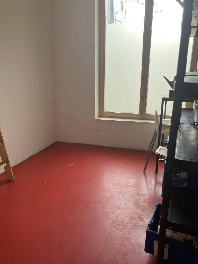 Leerer Lagerraum mit rotem Boden und einem Fenster, das Tageslicht hereinlässt, einfach und funktional.