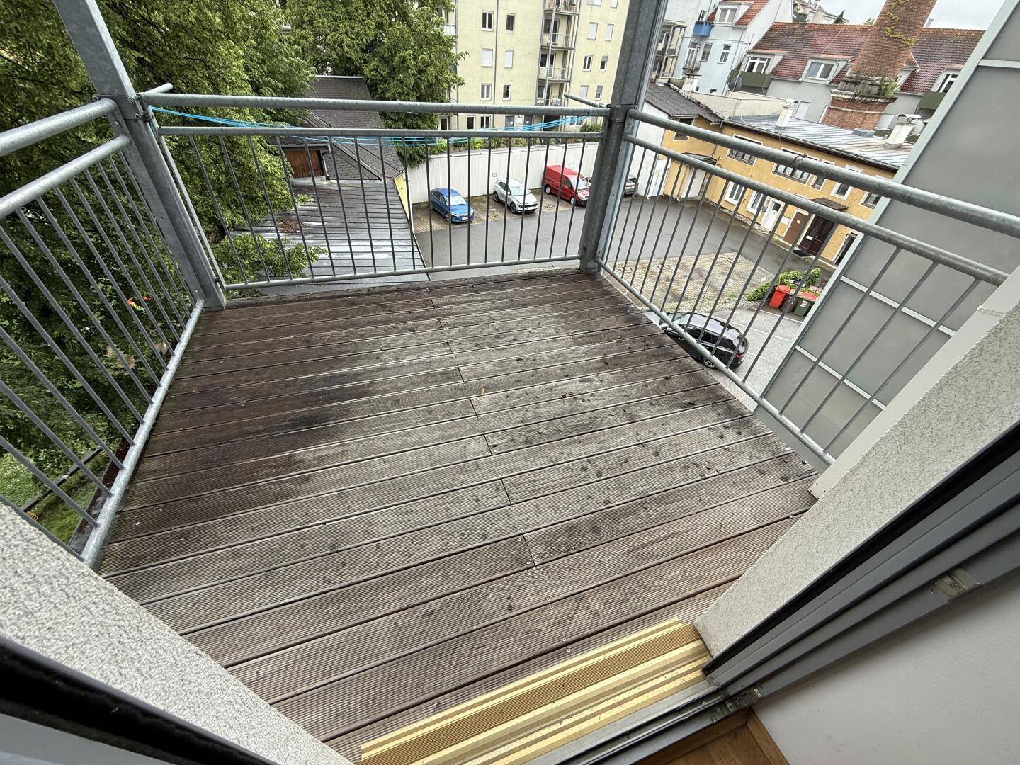 Kleiner Balkon mit Holzdielen und Blick auf den Innenhof und umliegende Gebäude.