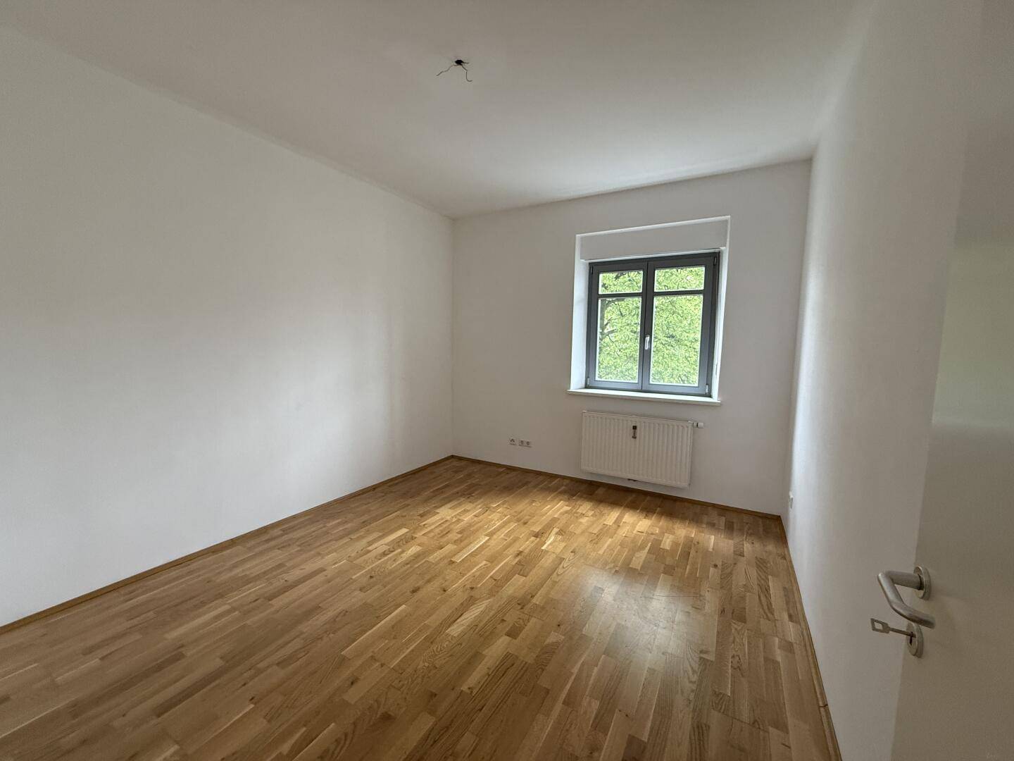 Helles und leeres Zimmer mit Holzboden und einem Fenster, das eine angenehme Atmosphäre schafft.