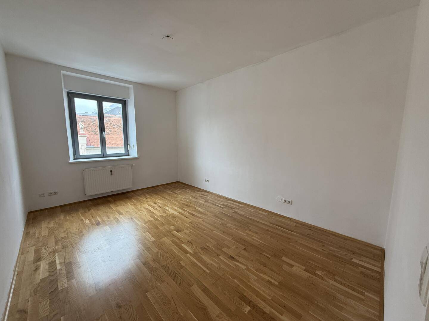 Geräumiges Zimmer mit Parkettboden und Fenster, bereit für individuelle Gestaltung.