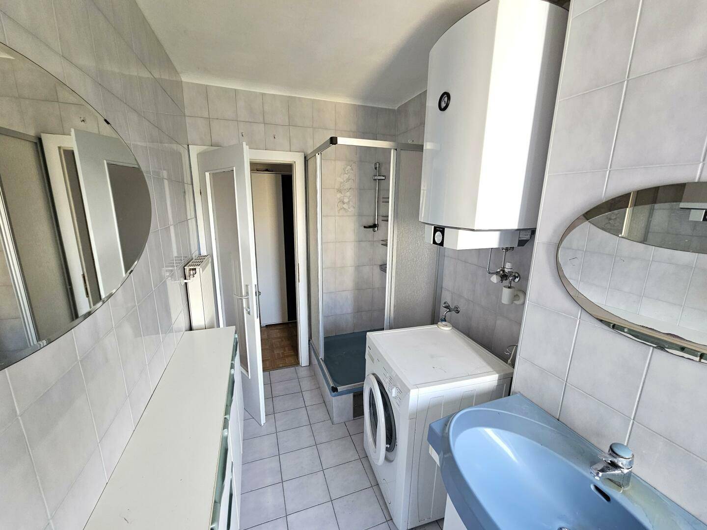 Funktionales Badezimmer mit Duschkabine, Waschmaschine und einem Spiegel über dem Waschbecken.