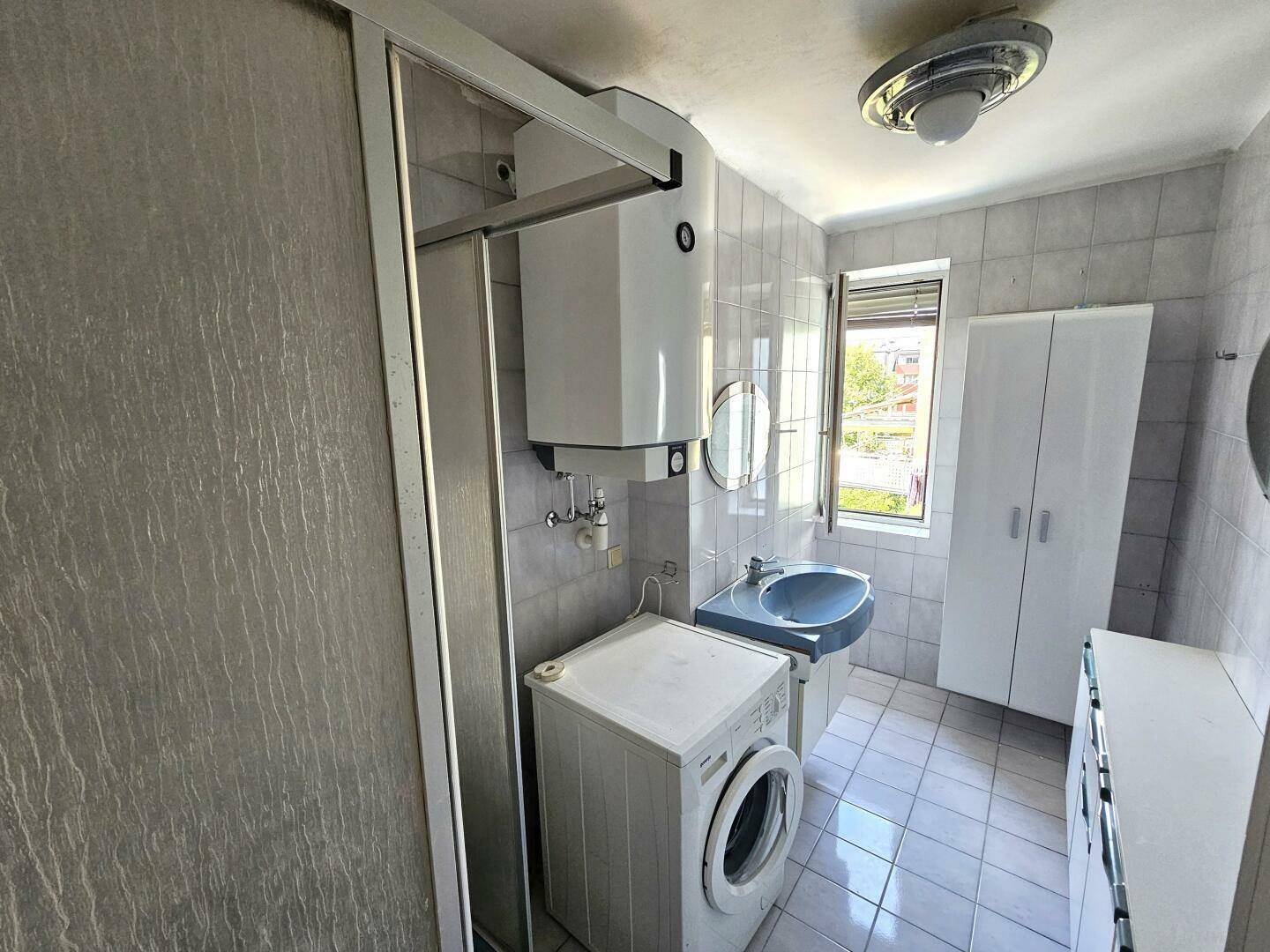 Badezimmer mit Dusche, Waschmaschine, blauem Waschbecken und Fenster für natürliche Belüftung.