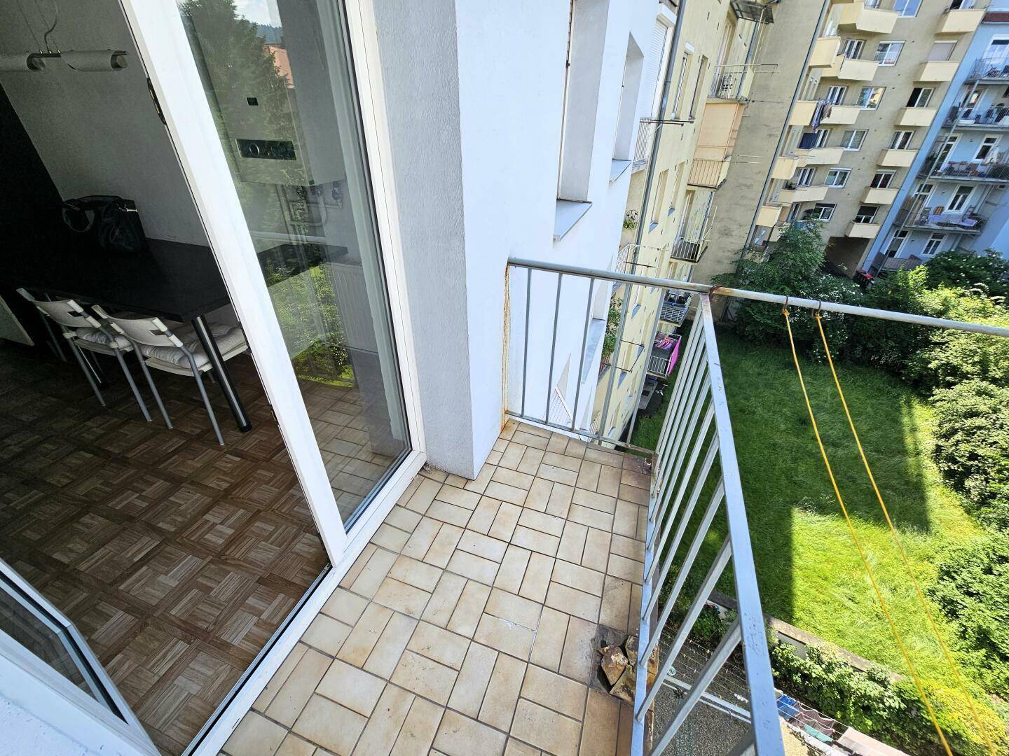 Kleiner Balkon mit Fliesenboden und Blick auf den Innenhof und umliegende Gebäude.