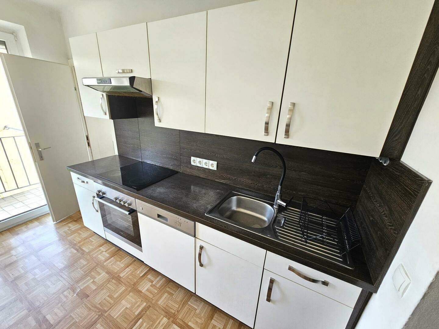 Moderne Einbauküche mit weißen Schränken, dunkler Arbeitsplatte und Spülbecken.