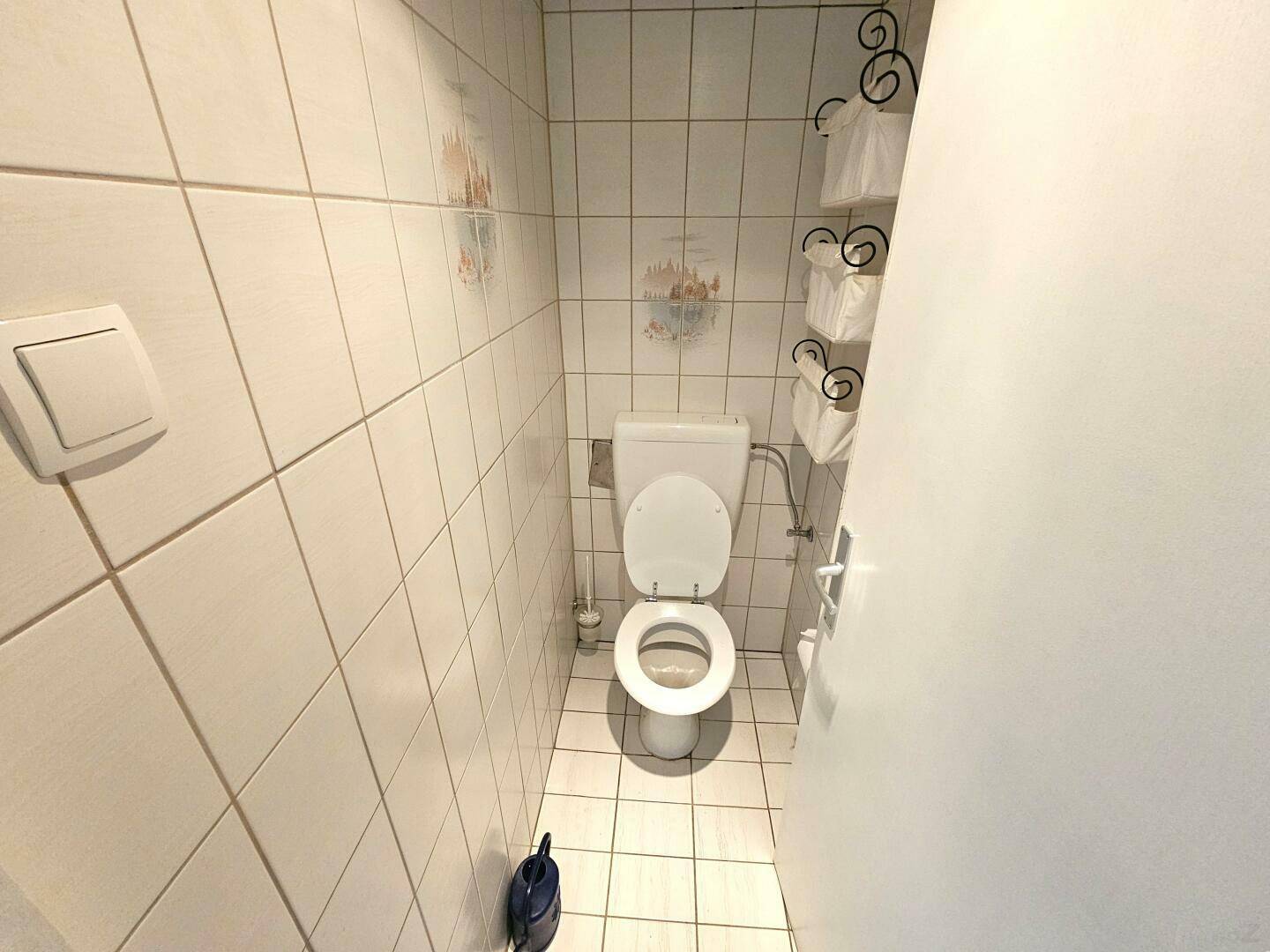 Separate Toilette mit weißen Fliesen und einem Wand-WC in einem kleinen Raum.