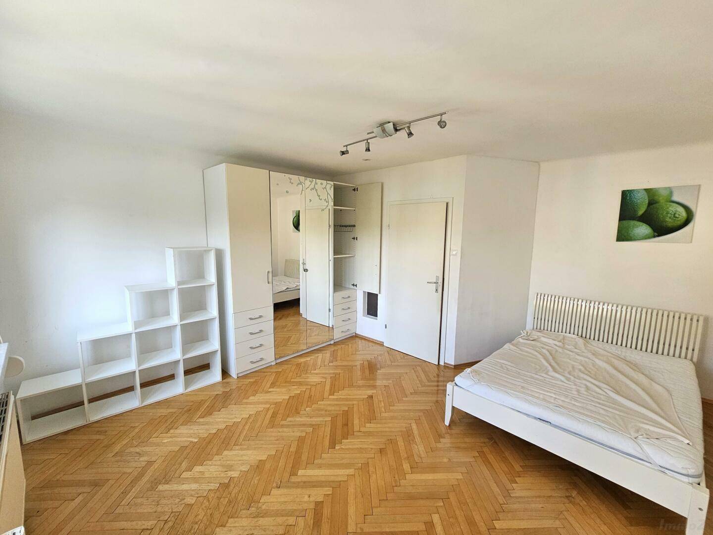 Schlafzimmer mit Parkettboden, weißem Kleiderschrank mit Spiegeltüren und einem Bett.