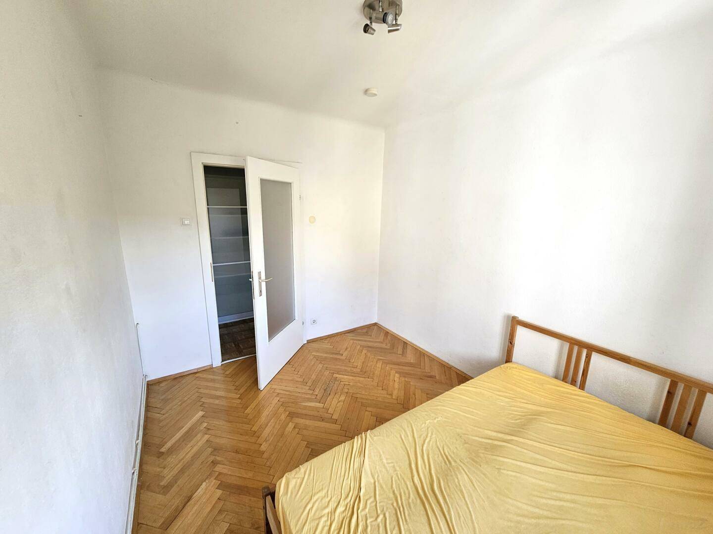 Helles Schlafzimmer mit Parkettboden und Zugang zu einem angrenzenden Abstellraum.