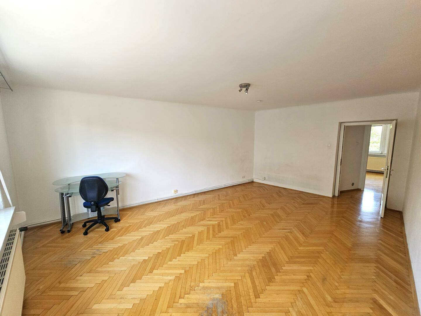 Großes Wohnzimmer mit Parkettboden, Fenster und einem Schreibtisch in der Ecke.