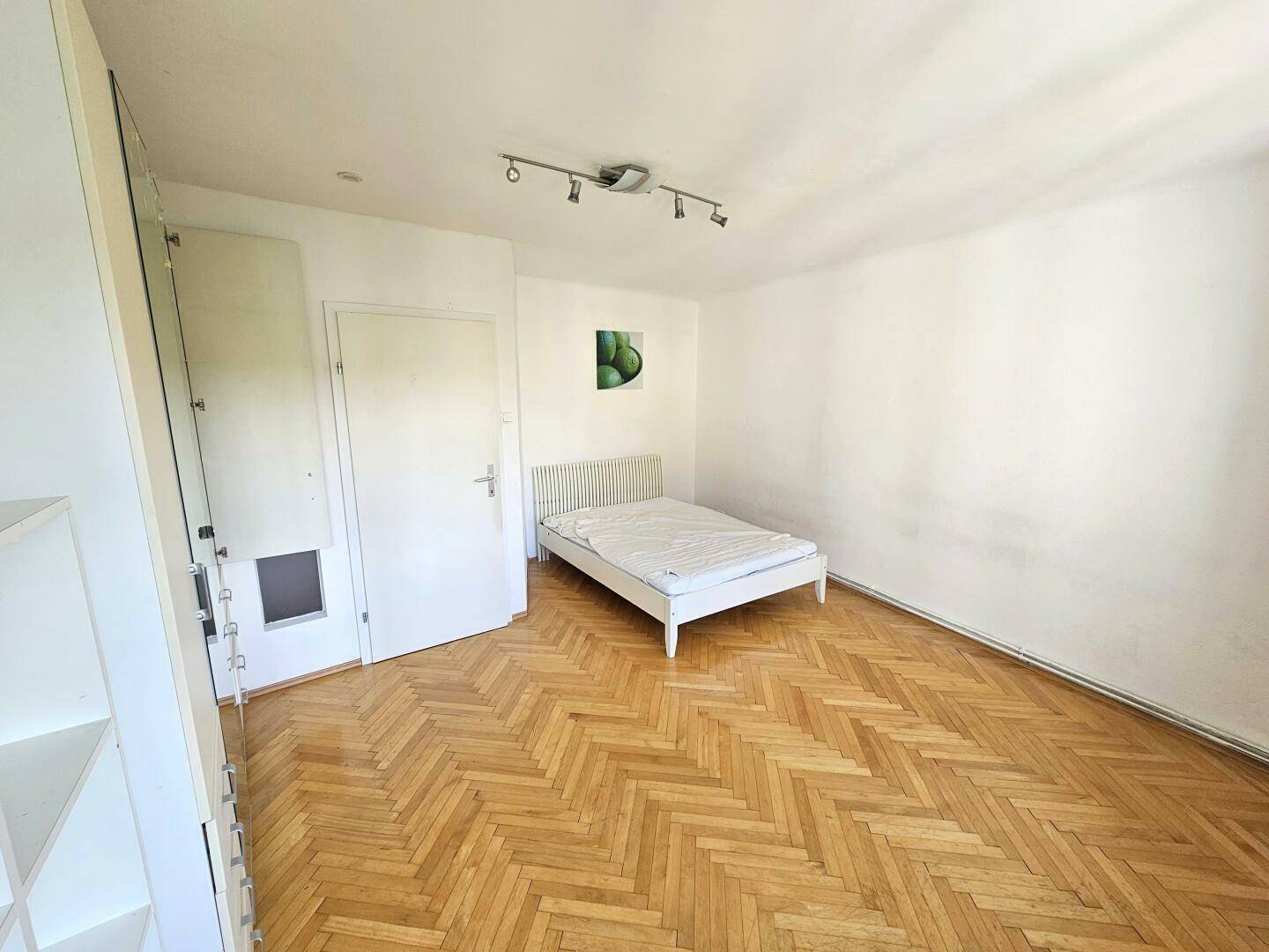 Schlafzimmer mit weißem Bett, Parkettboden und einem dekorativen Bild an der Wand.