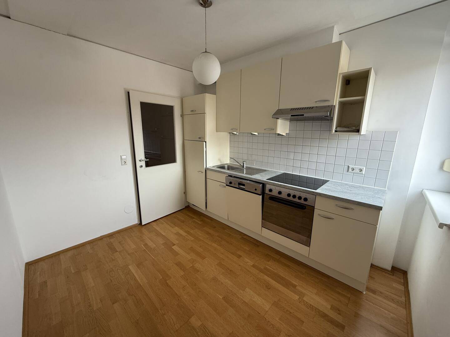 Funktionale Einbauküche mit hellen Schränken, Fliesenrückwand und Parkettboden.